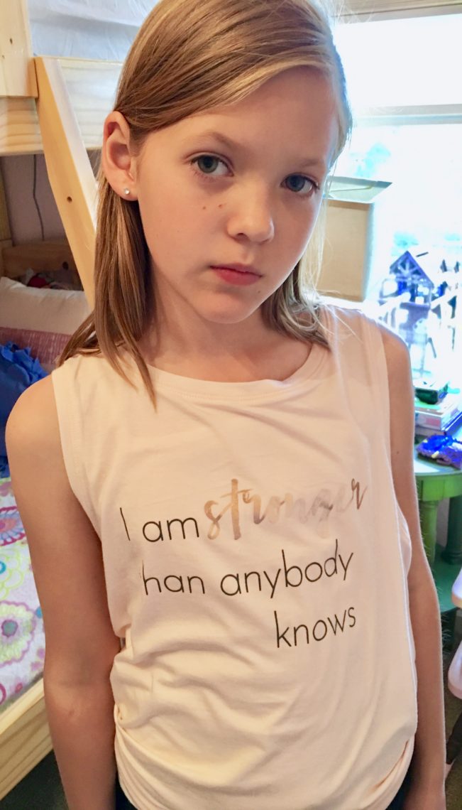 A little girl wears a t-shirt stating she is strong