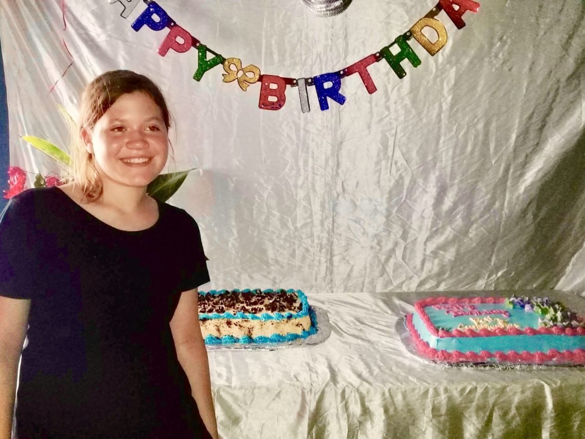 A young girl poses in front of cakes and Happy Birthday sign