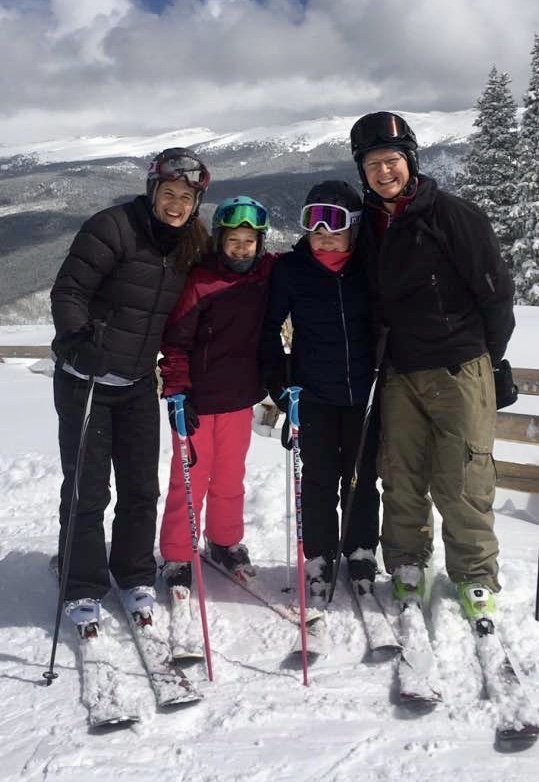 A family on a ski trip smiles from the top of a mountain