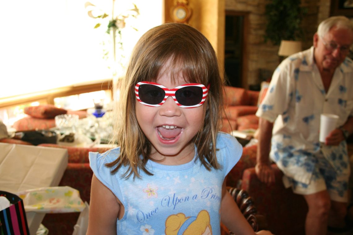 A young girl smiles bravely in striped sunglasses
